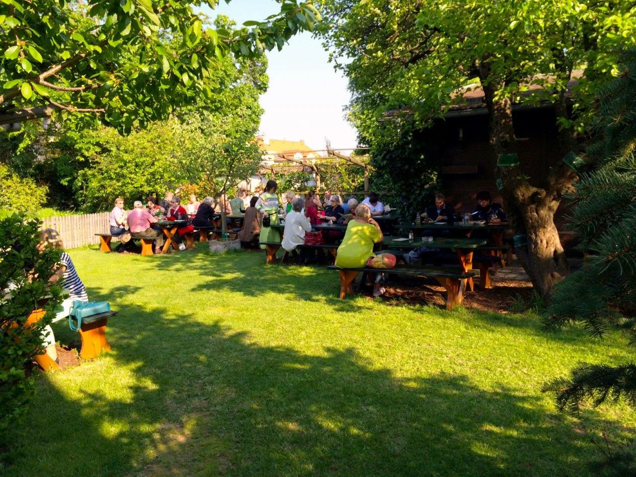 Besetzte Tischreihen im Gastgarten unter den alten Bäumen