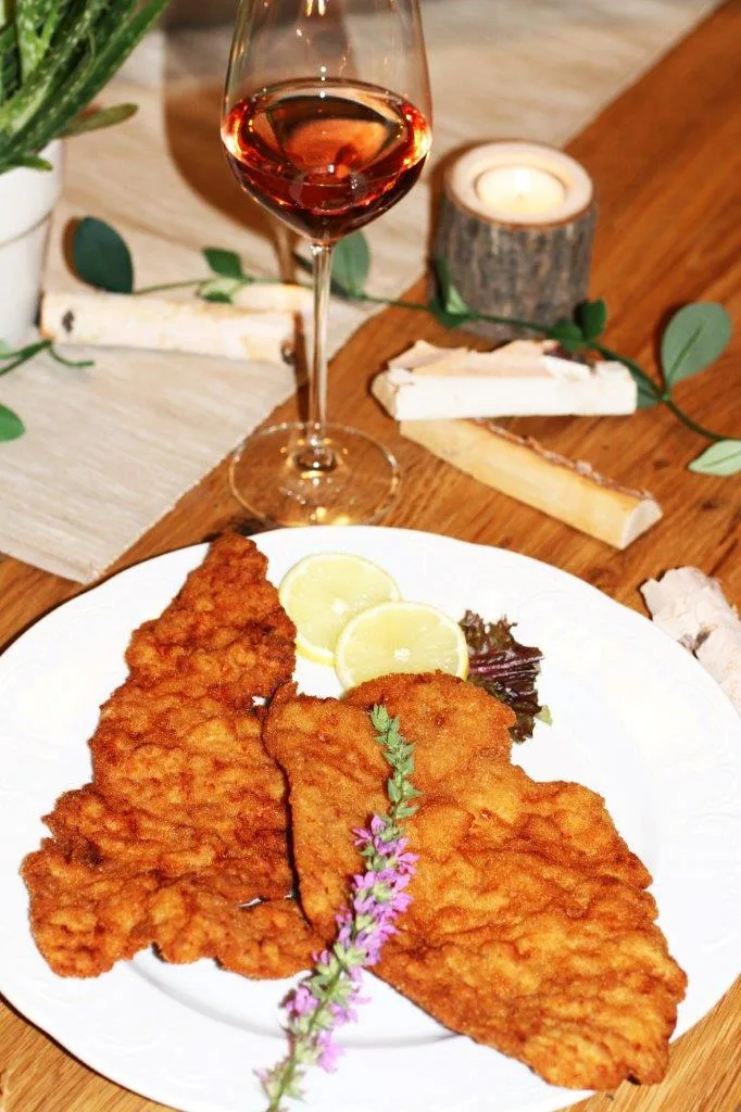 Wiener Schnitzel vom Schwein mit Zitronenscheiben, daneben ein Glas Wein