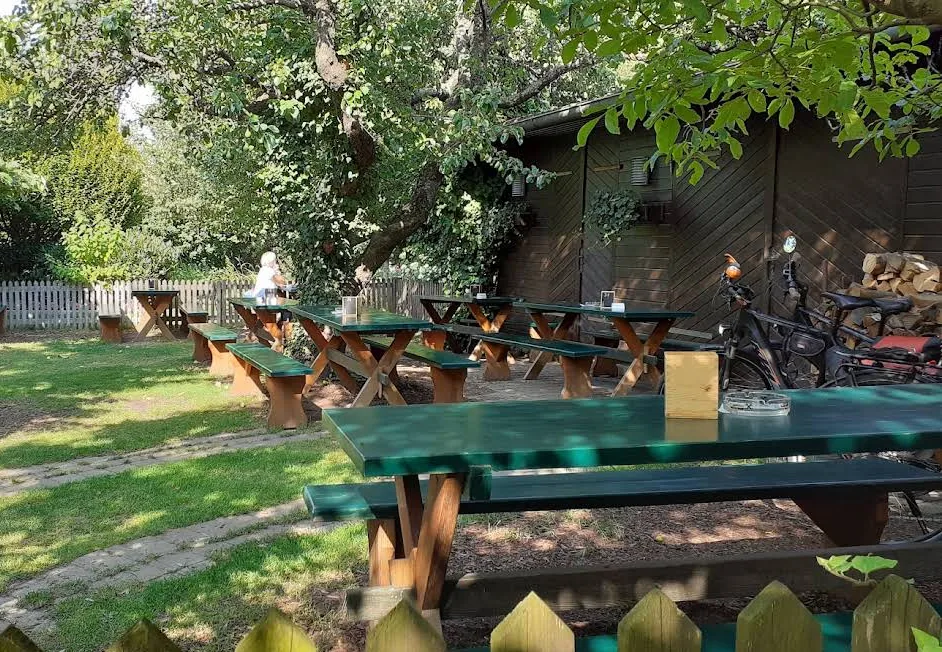 Gastgarten mit Tischreihen auf der Wiese, dahinter ein Holzgebäude