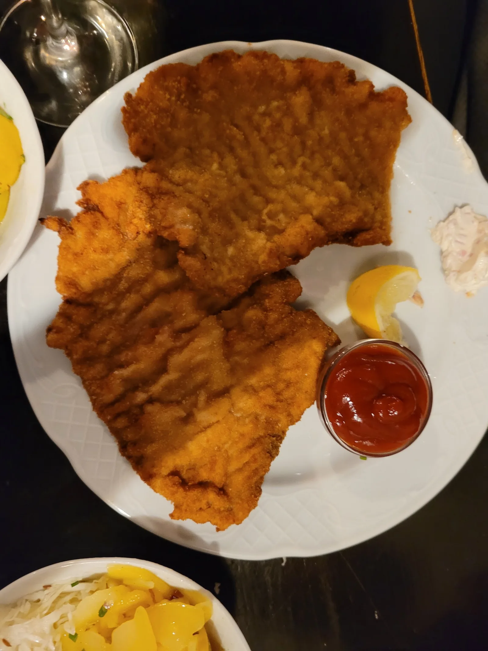 Zwei panierte Schnitzel mit Zitrone und Ketchup, daneben eine Schale Erdäpfel- und Krautsalat