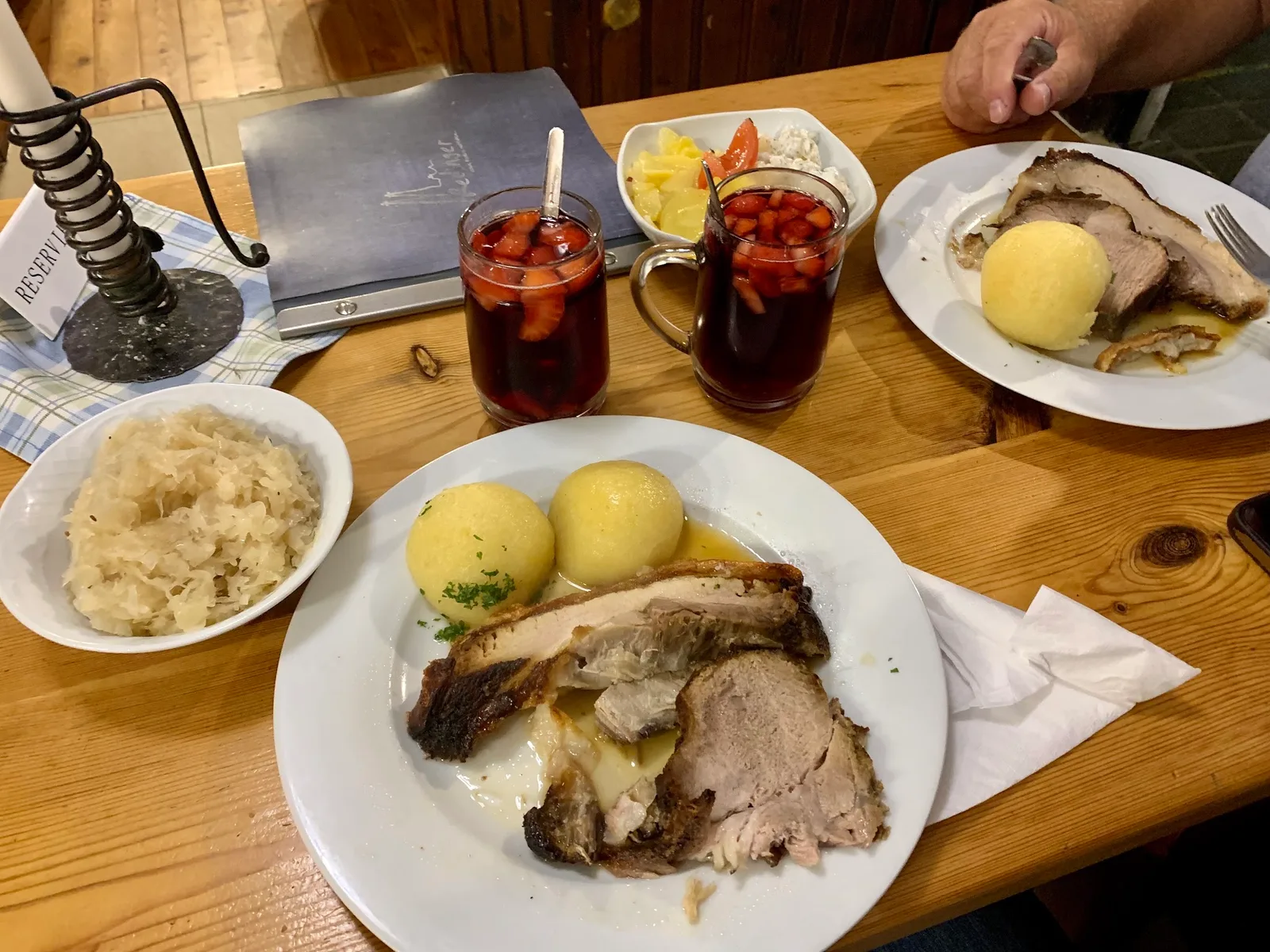 Gedeckter Tisch mit Schweinsbraten, Semmelknödeln, Sauerkraut und zwei Gläsern mit einem roten Getränk mit Erdbeeren